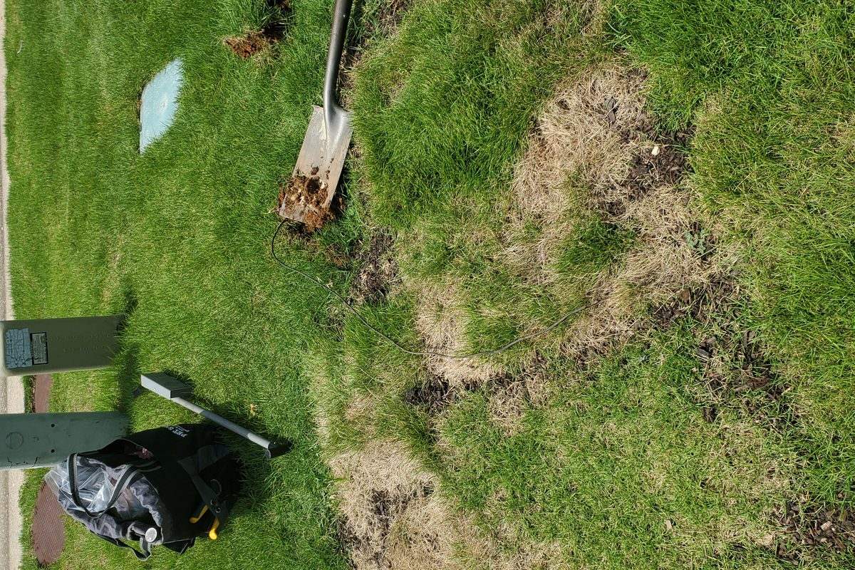 Dug section of lawn beside a buried utility marker post where the boundary wire was cut