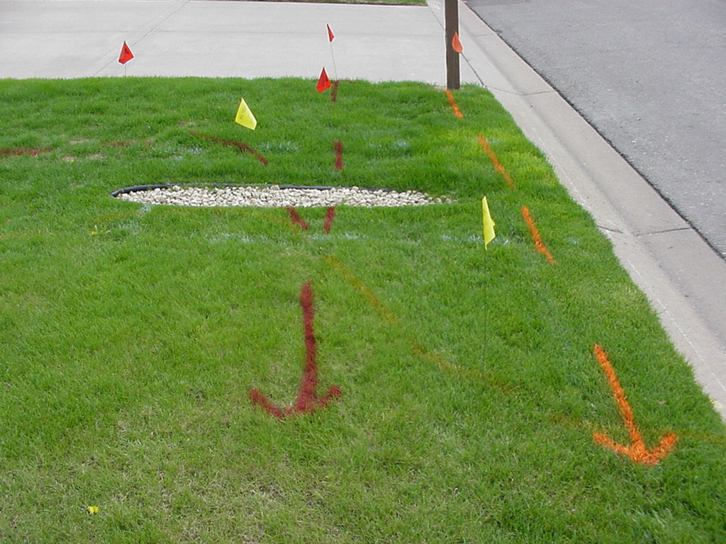 A front yard marked before digging, with red, orange and yellow utility flags and matching spray-painted arrows on the grass